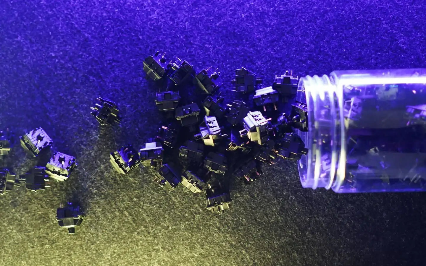 Czarne przełączniki mechaniczne do klawiatury wysypujące się z przezroczystego pojemnika na ciemnym tle