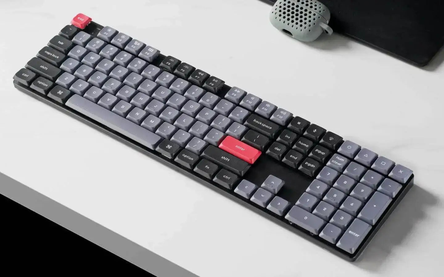 nowoczesna klawiatura mechaniczna z czarnymi i szarymi klawiszami oraz czerwonymi enter i escape na białym biurku