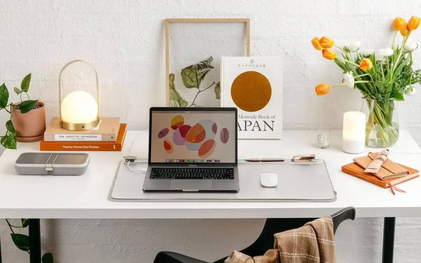 Minimalistyczne biurko z laptopem MacBook, rośliną, lampą, książkami, tulipanami i akcesoriami do pisania