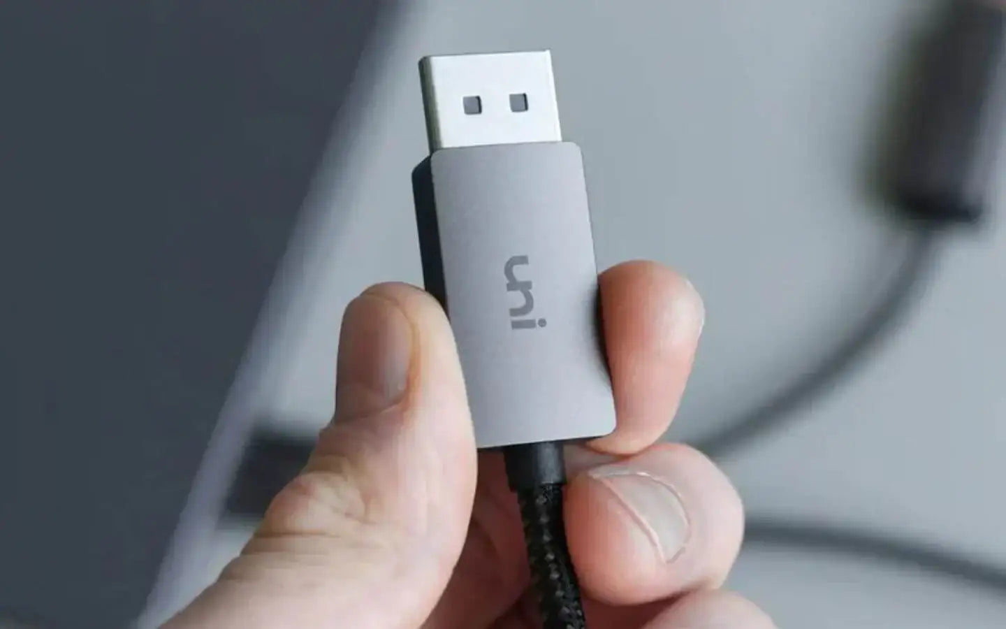 Ręka trzymająca szary kabel USB z logo uni na tle rozmytego biurka