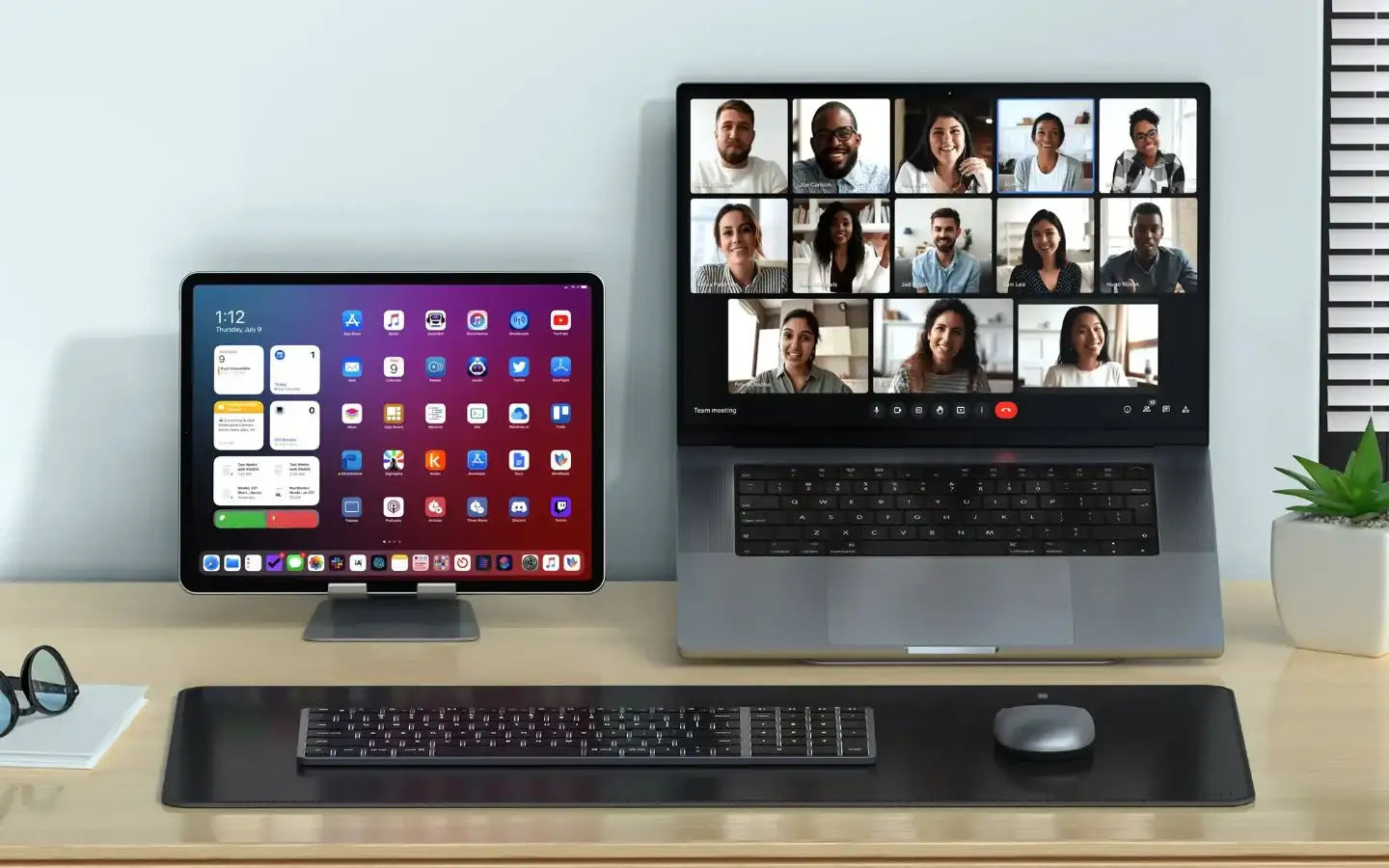 Wideokonferencja na laptopie z wieloma uczestnikami, obok tablet na biurku z aplikacjami