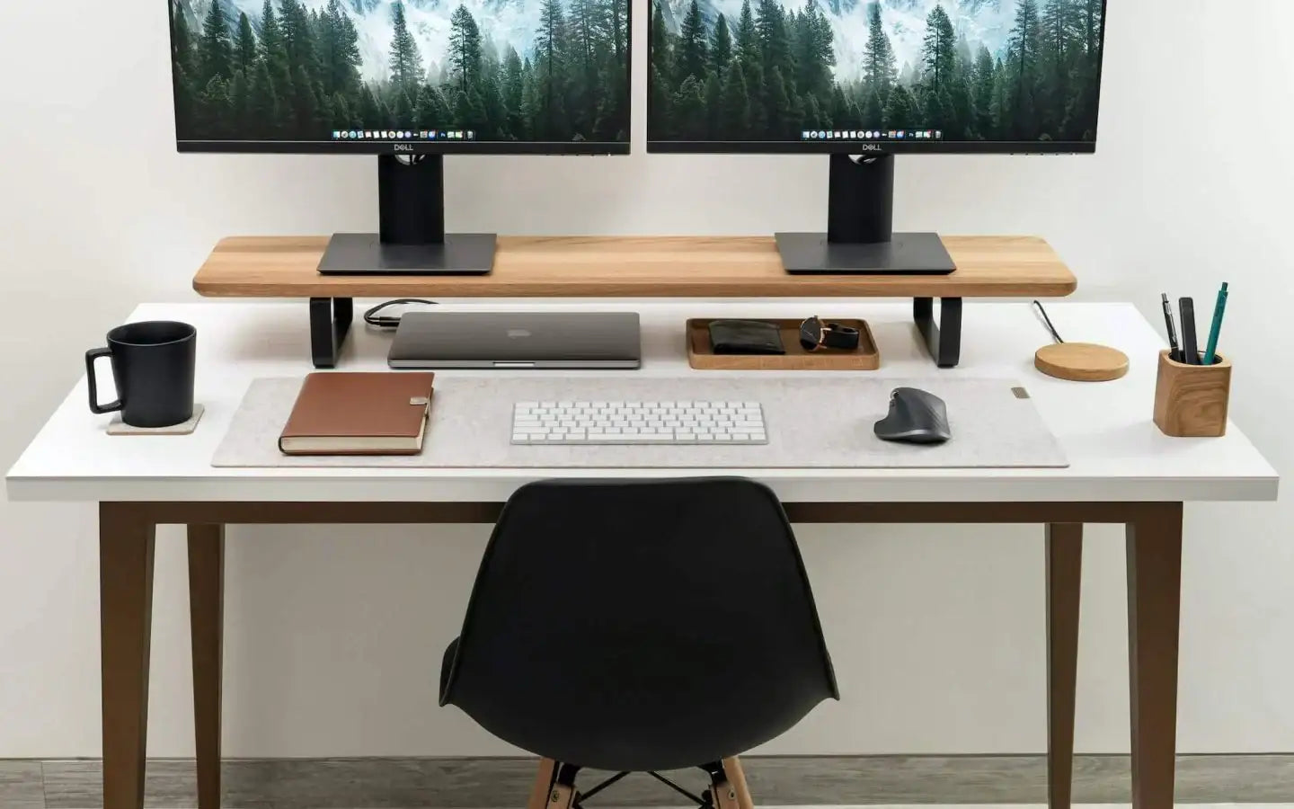 Minimalistyczne biurko z dwoma monitorami, laptopem, klawiaturą i akcesoriami do pracy.