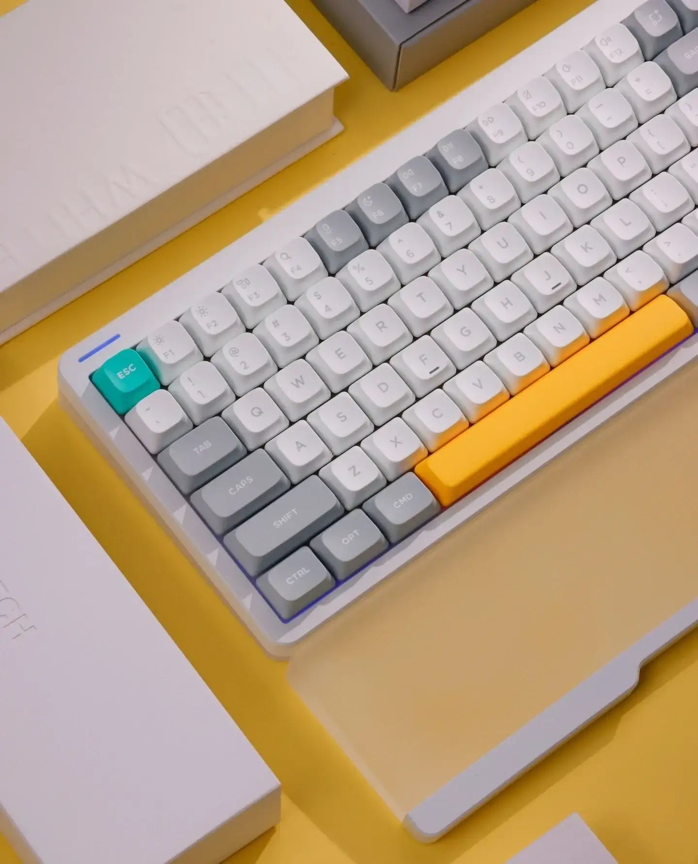 Klawiatura mechaniczna z białymi, szarymi i żółtymi klawiszami na żółtym tle, obok biały notes i opakowanie