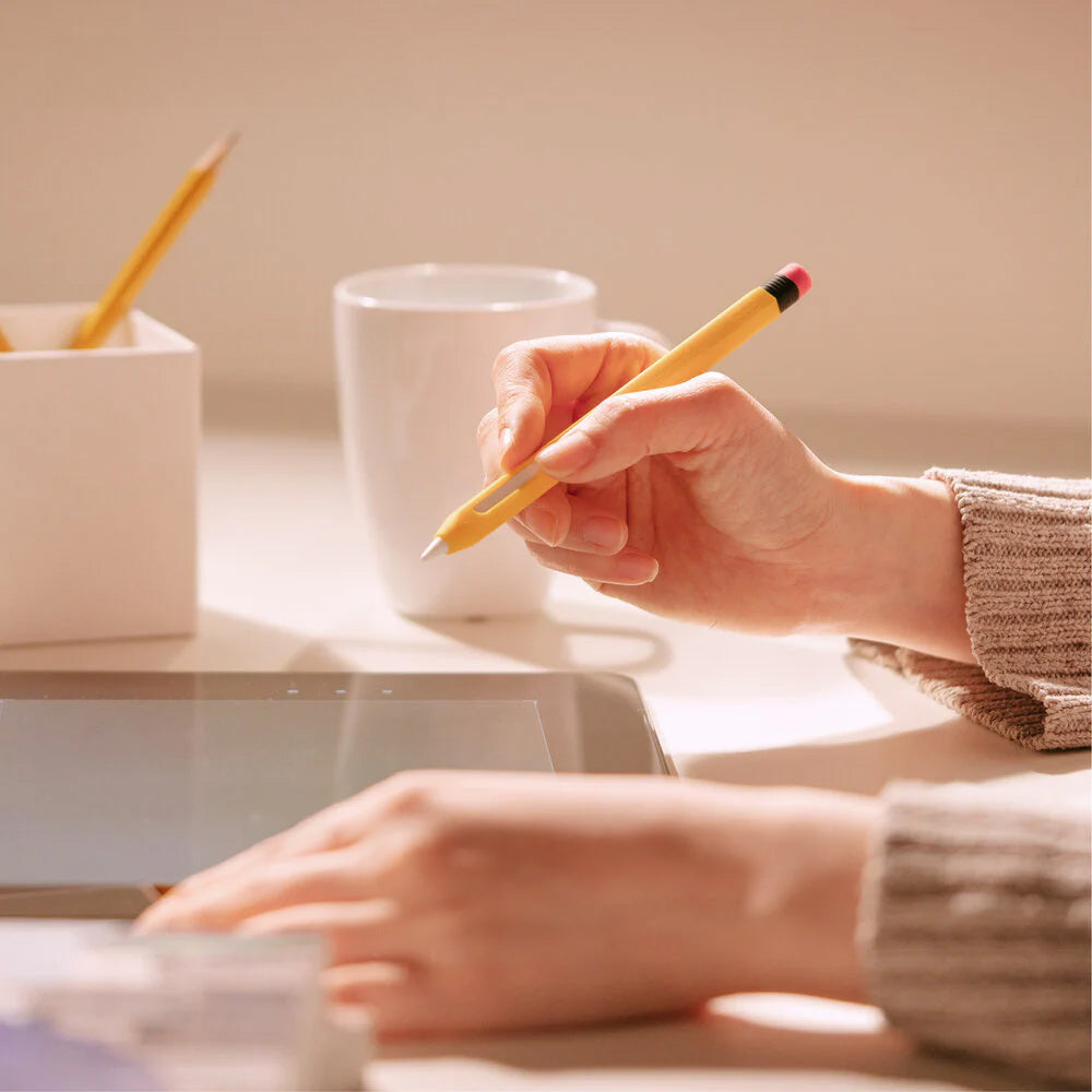 Apple Pencil w żółtym etui, tablet, kubek i ołówek na biurku w świetle dziennym