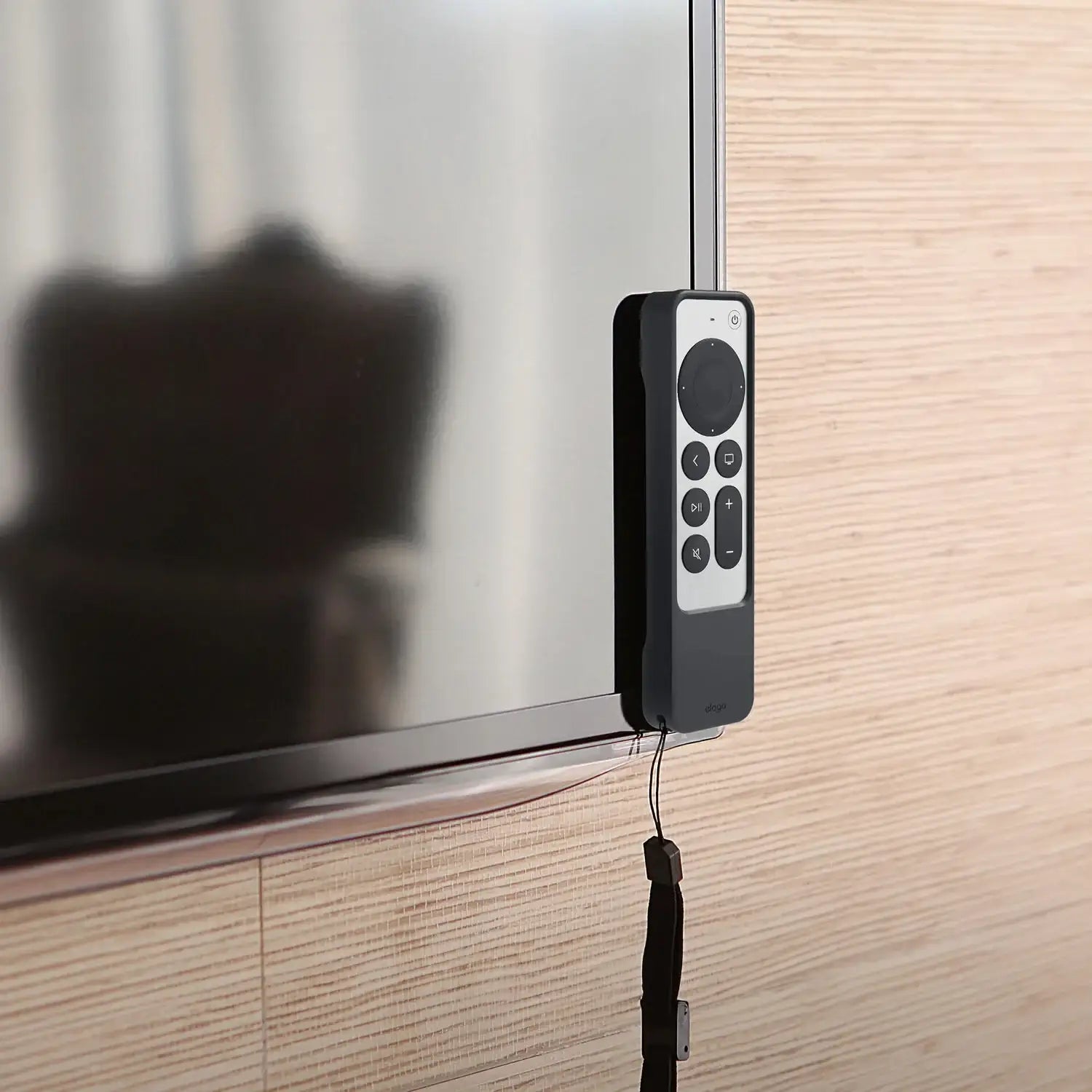Pilot Apple TV w magnetycznym czarnym etui mocowanym do krawędzi telewizora na jasnej ścianie