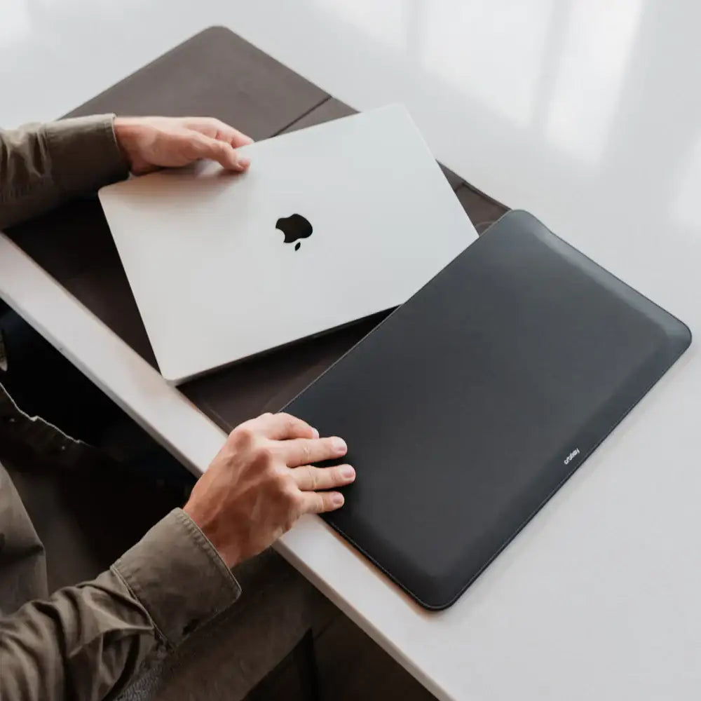Osoba wkłada srebrnego MacBooka do eleganckiego czarnego etui na biurku