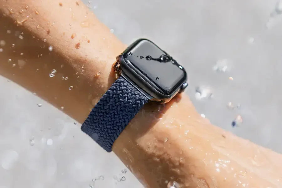 Wodoodporny smartwatch z granatowym paskiem na nadgarstku, zachlapany wodą