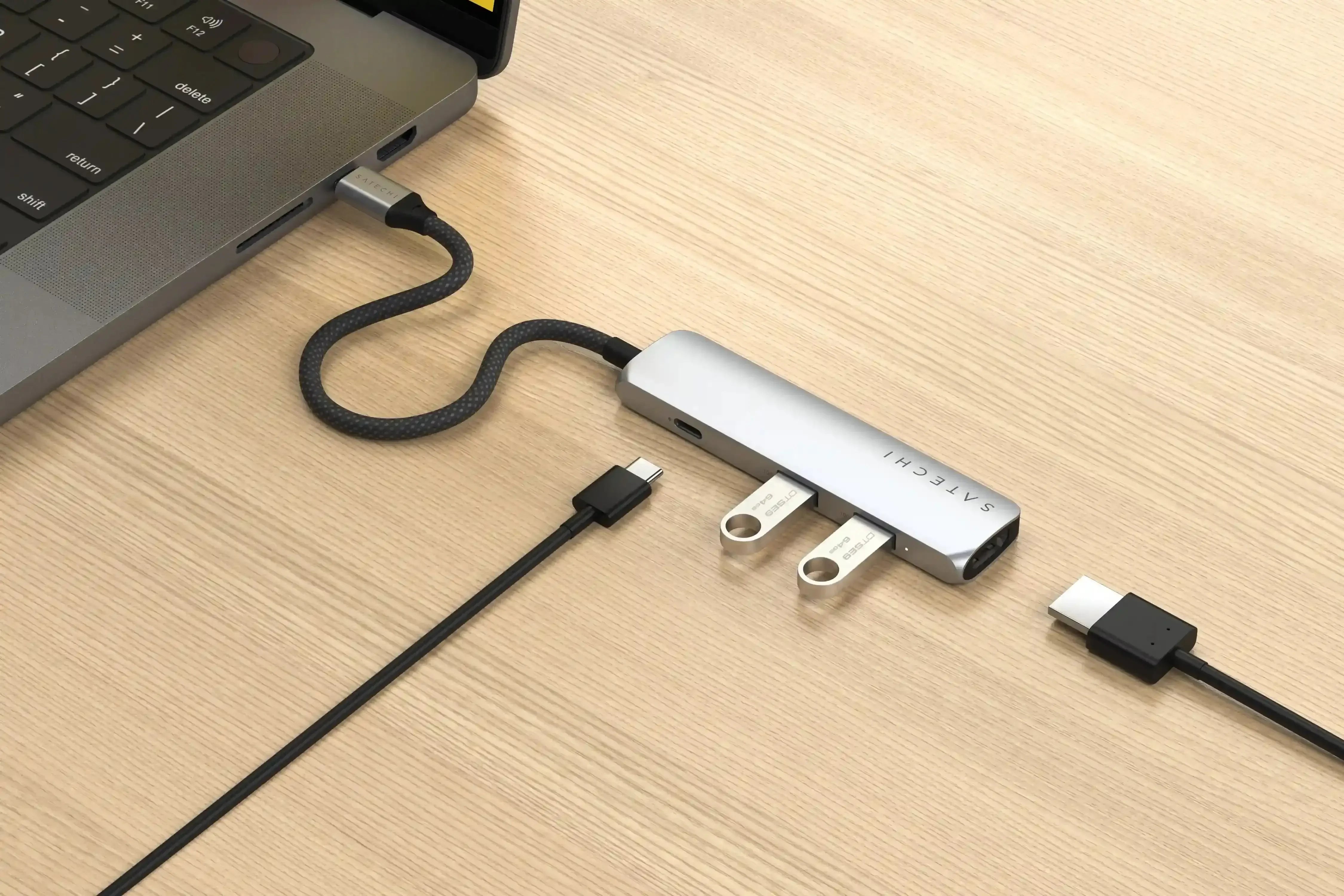 Srebrny adapter USB-C 4w1 podłączony do laptopa na drewnianym biurku, widoczne złącza USB i HDMI