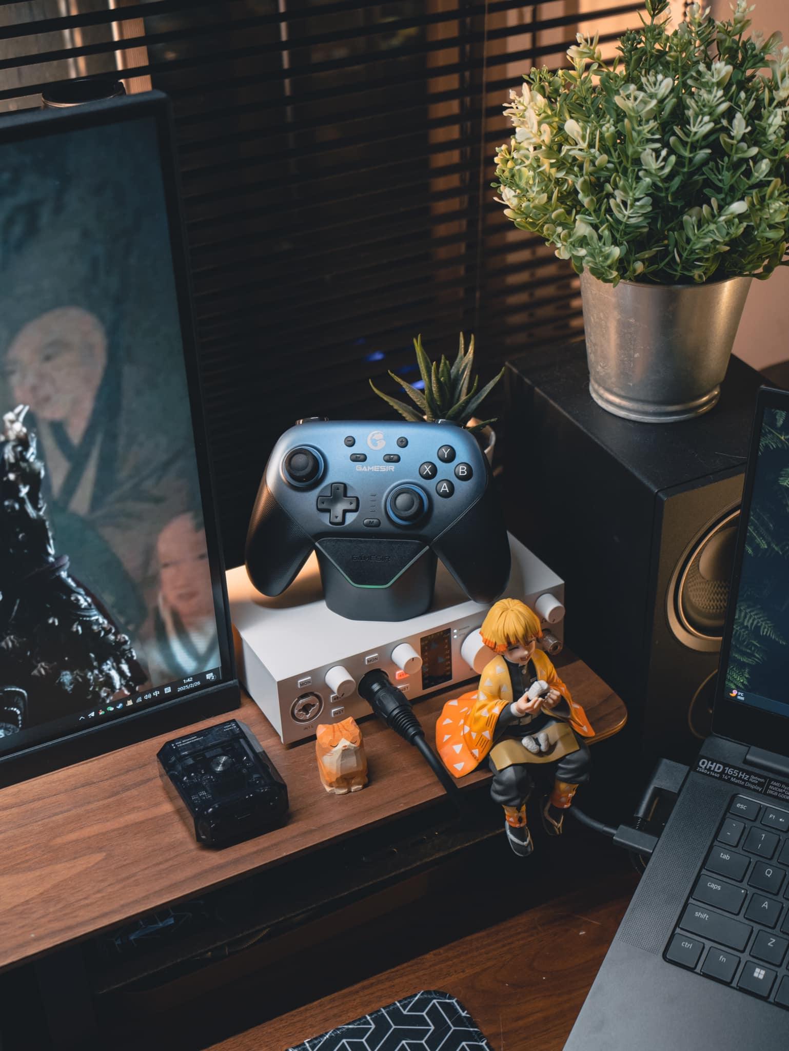 Gra wideo z kontrolerem Gamesir na biurku z laptopem, figurką i rośliną – idealny setup gamingowy i biurowy