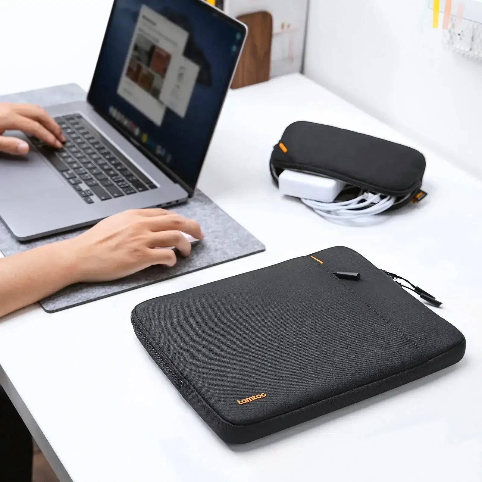 Czarna torba na laptopa i organizer na kable na biurku obok pracującej osoby, akcesoria do home office