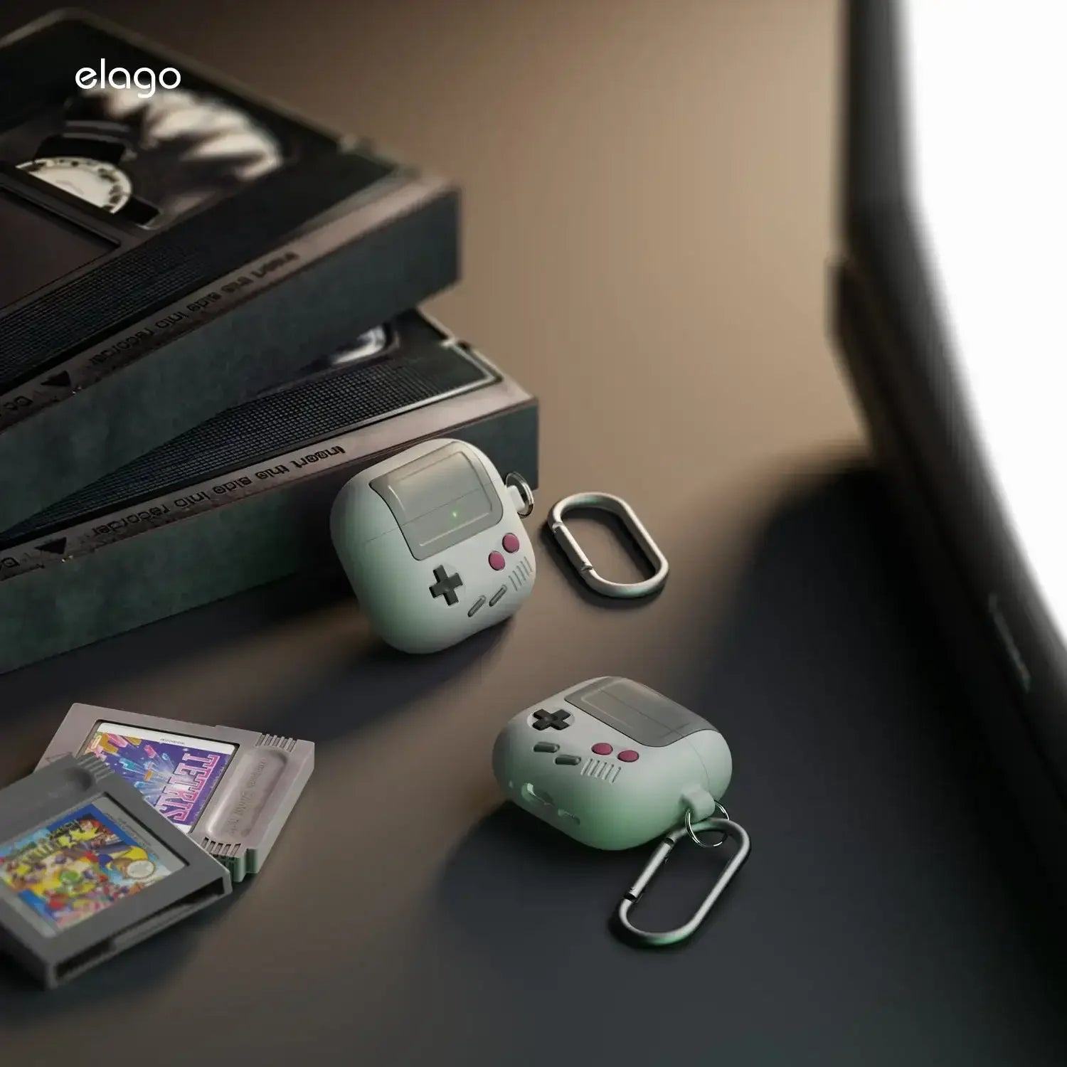 Etui na słuchawki w stylu retro jak konsola Game Boy, obok kartridży i kaset wideo na biurku.