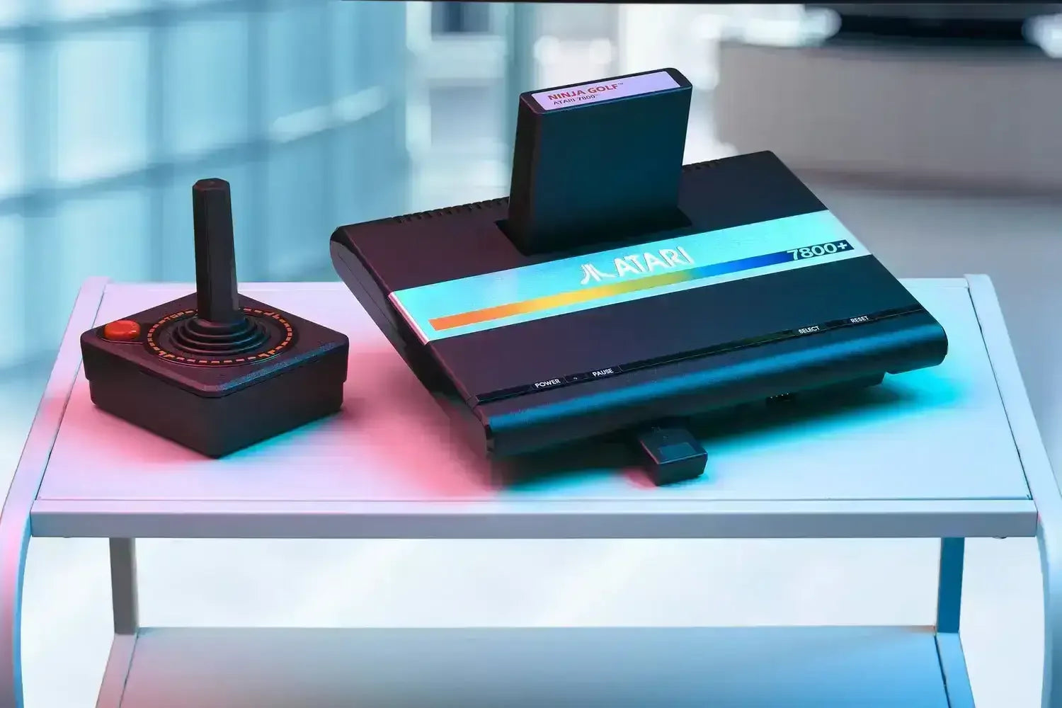Klasyczna konsola Atari 7800+ z joystickiem i grą Ninja Golf na białym stoliku