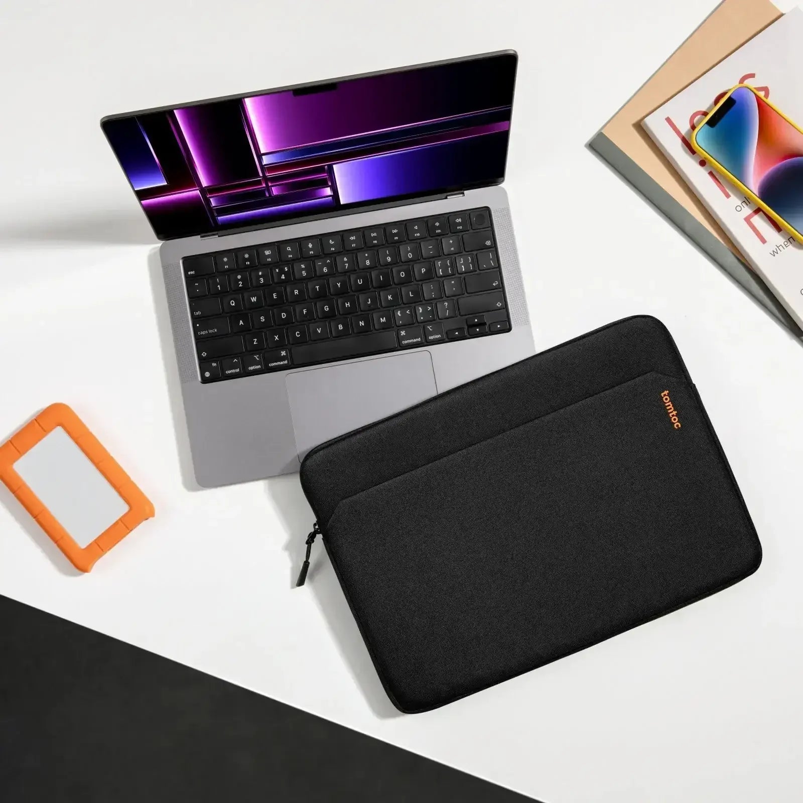 Nowoczesny laptop na biurku z etui, smartfonem i dyskiem przenośnym, idealny desk setup.