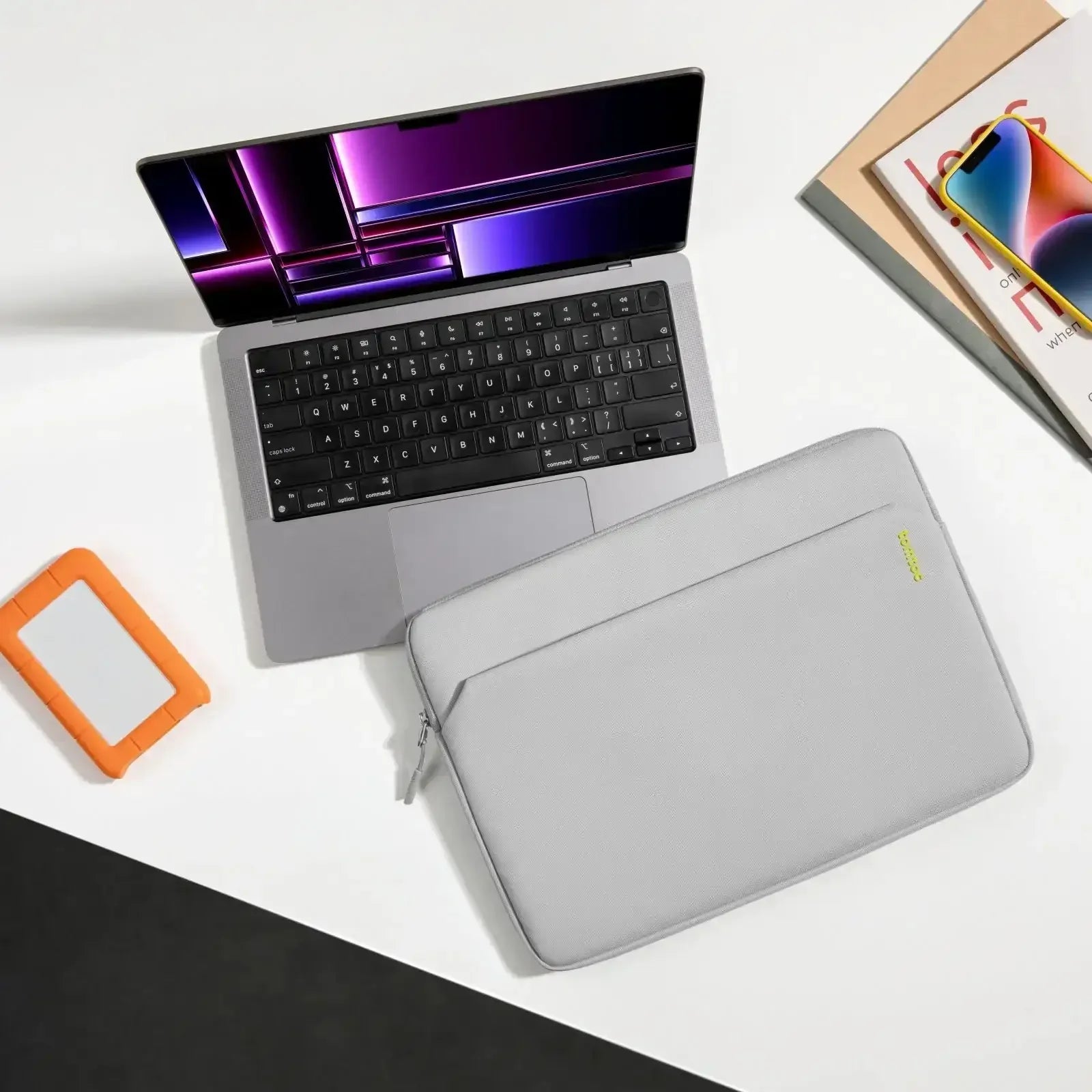 Nowoczesny laptop na biurku, szara torba na laptop, dysk zewnętrzny, czasopisma i smartfon