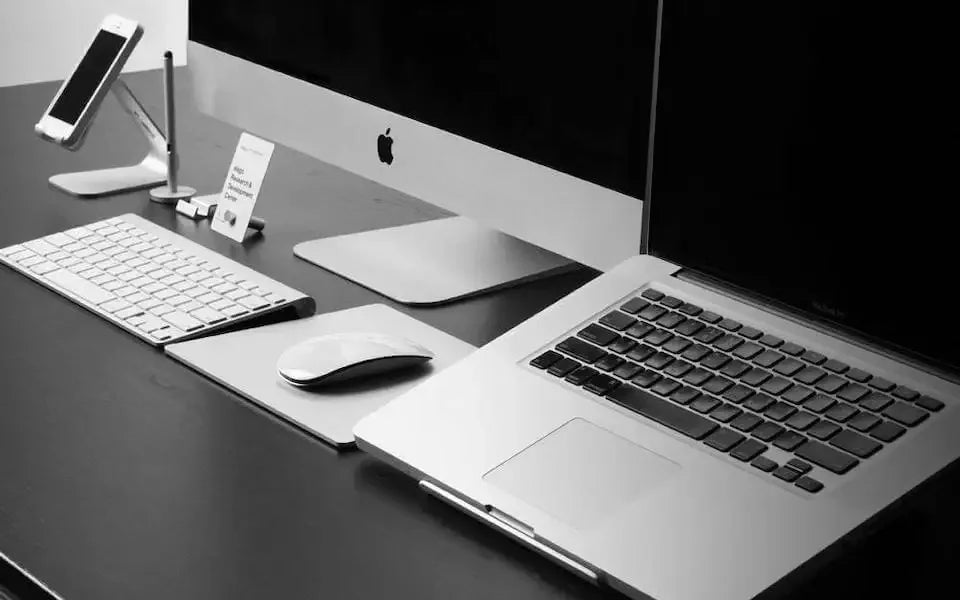 Minimalistyczny desk setup z klawiaturą, laptopem, monitorem, myszką i stojakiem na telefon