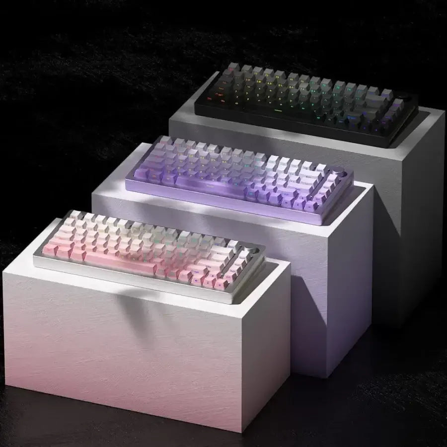 Trzy klawiatury mechaniczne RGB na białych blokach, różne kolory podświetlenia