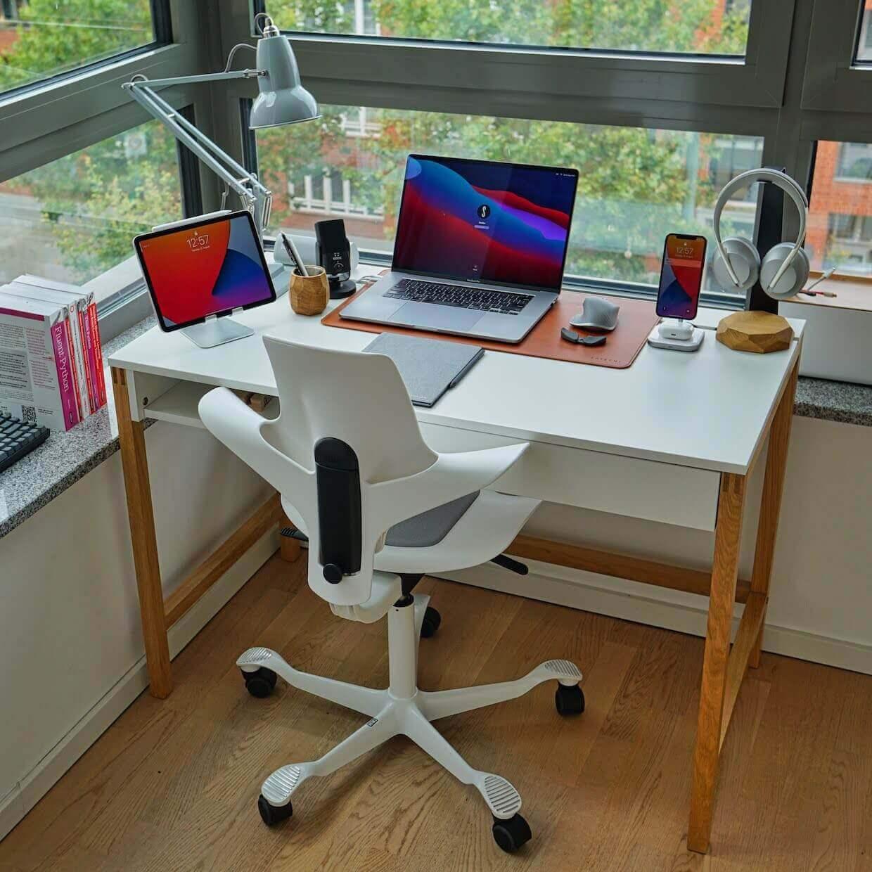 Nowoczesny desk setup z laptopem, tabletem, akcesoriami biurowymi i ergonomicznym krzesłem