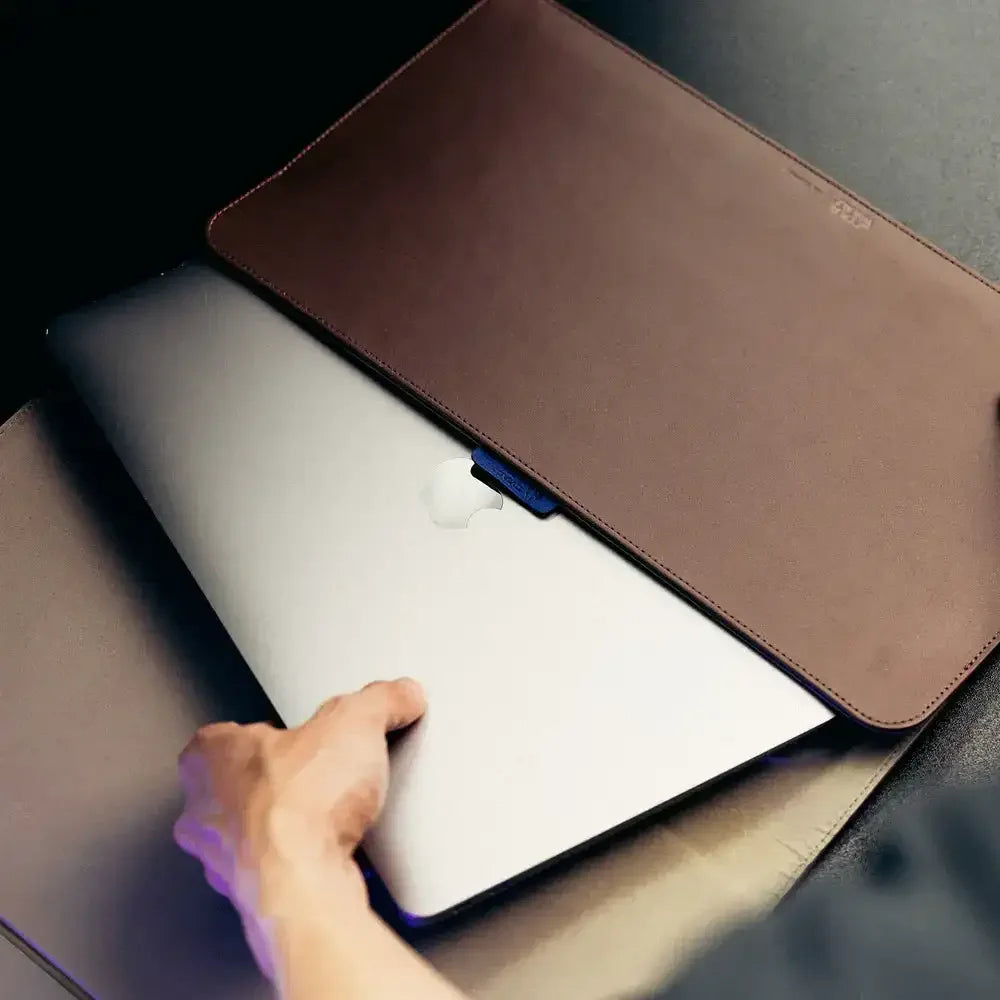 Ręka wsuwająca laptopa do skórzanego etui ochronnego na biurku, akcesoria do biura