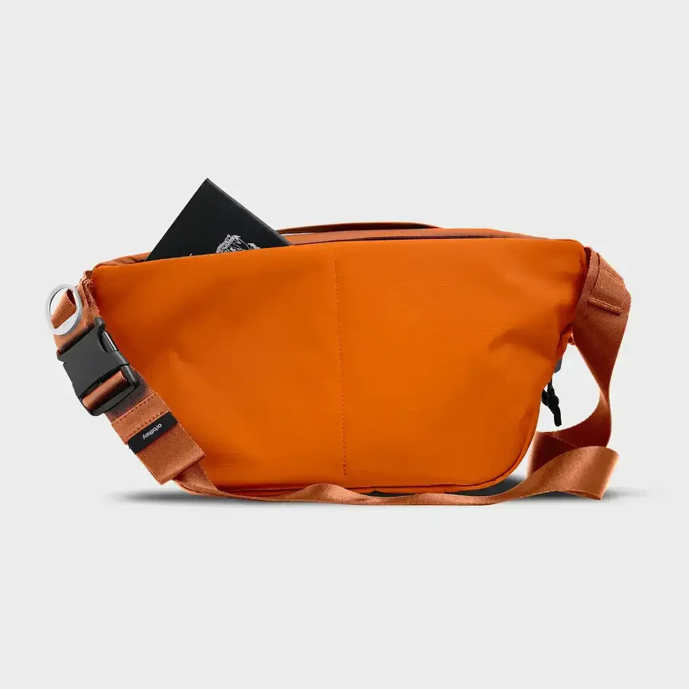 Pomarańczowa torba na ramię typu sling z czarnym notesem w środku, minimalistyczny design.