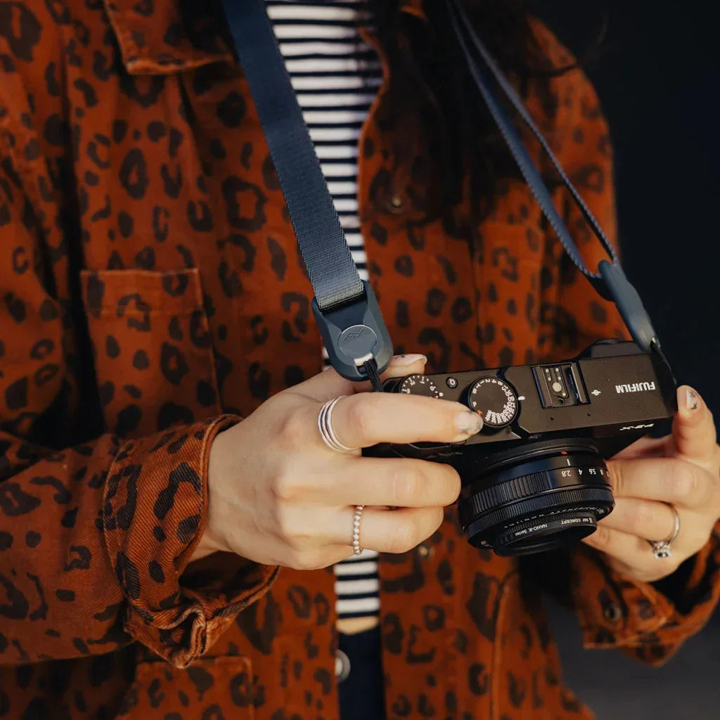 Kobieta w kurtce w panterkę trzyma czarny aparat Fujifilm z obiektywem, gotowa do robienia zdjęć.