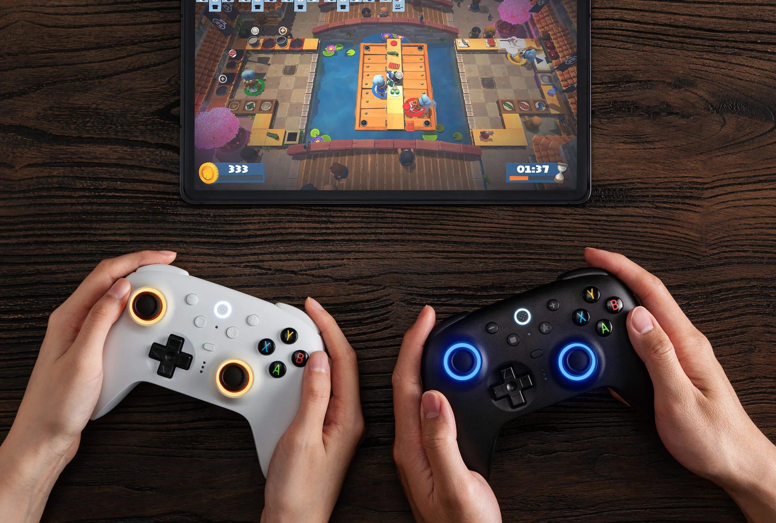 Dwa kontrolery do gier z podświetleniem, biały i czarny, w rękach, przed tablet z grą