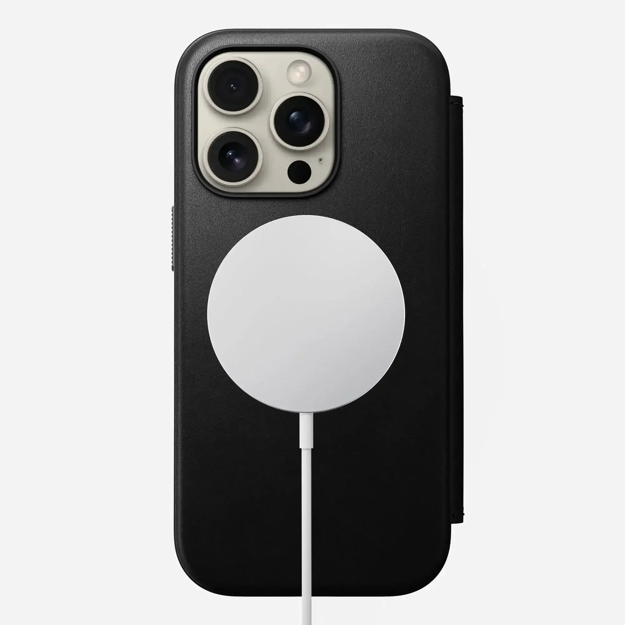 iPhone z czarnym etui, ładowany bezprzewodową ładowarką MagSafe na białym tle