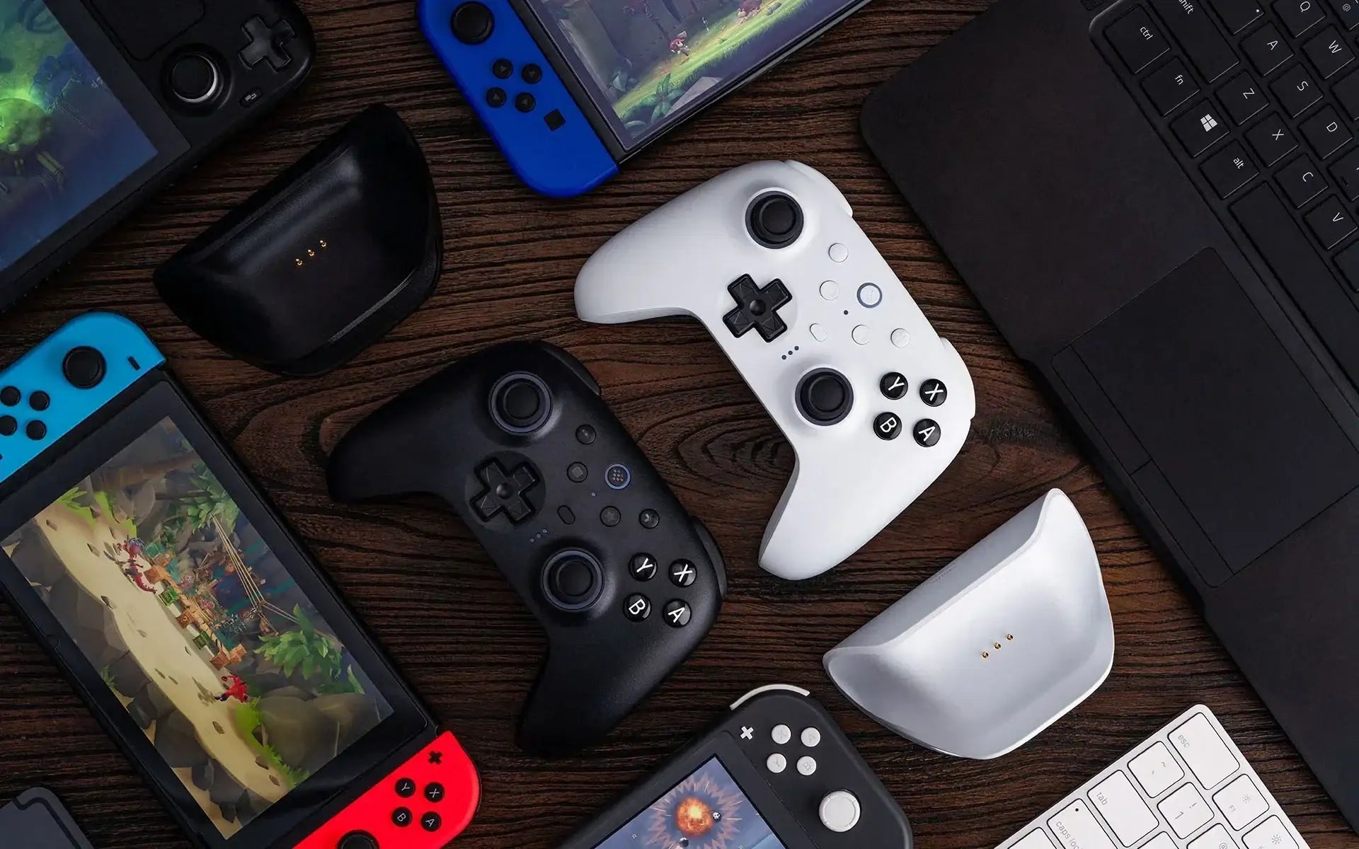 Białe i czarne kontrolery do gier, konsole przenośne, laptop, klawiatura na drewnianym stole
