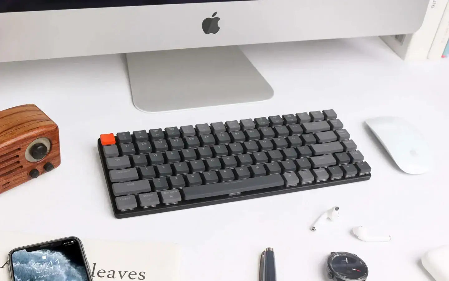 Biały biurkowy zestaw z iMakiem, szarą klawiaturą mechaniczną, białą myszką, drewnianym radiem i słuchawkami AirPods