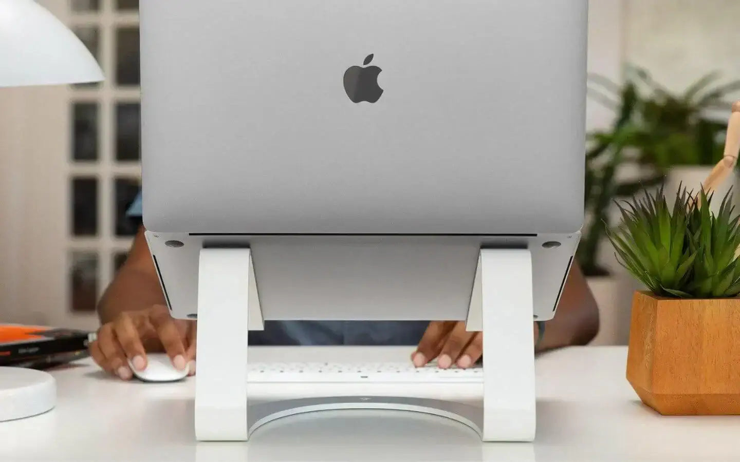 Silver MacBook na białym stojaku z rękami używającymi białej klawiatury i myszy na białym biurku