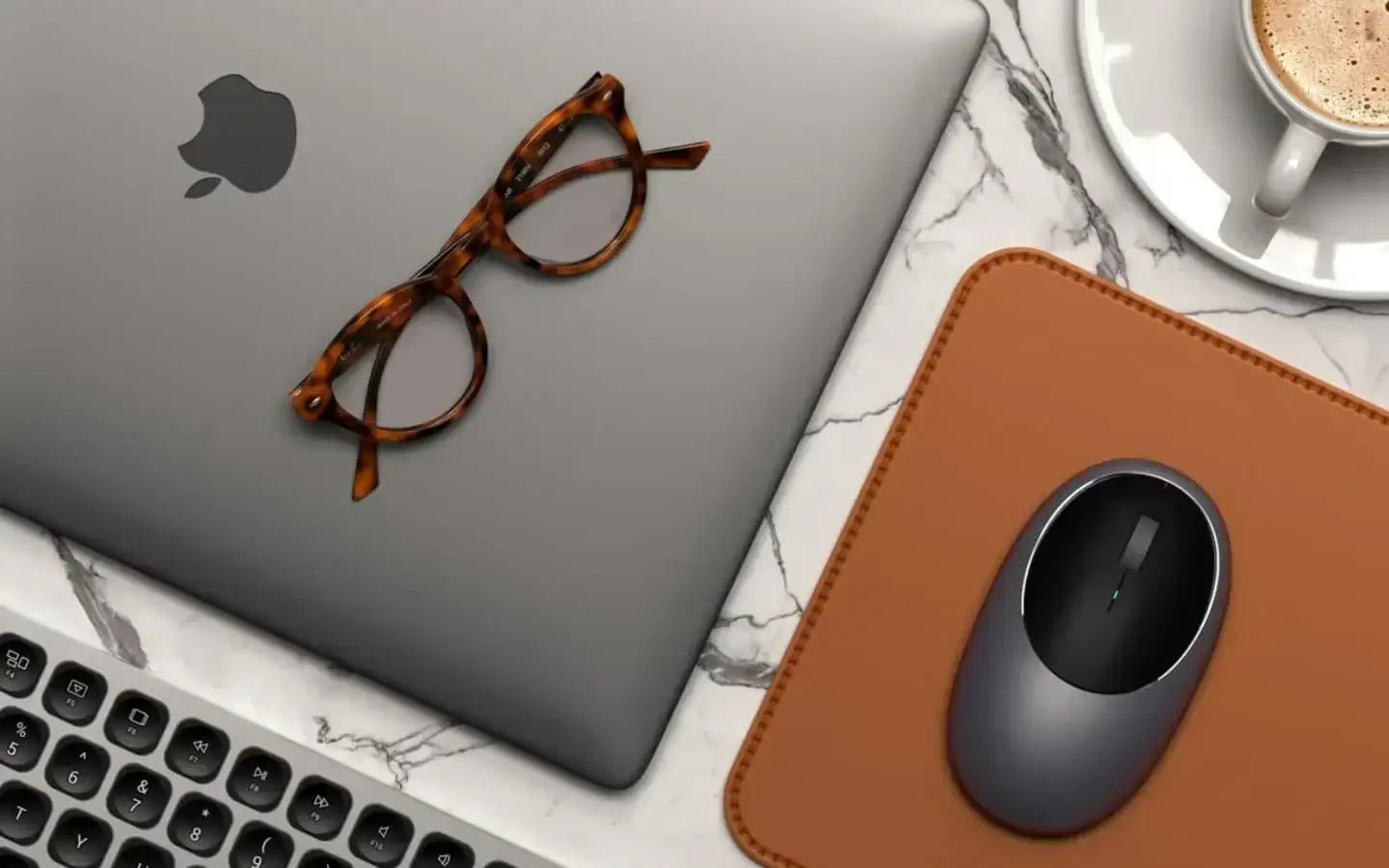 Nowoczesne biurko z laptopem Apple, okularami, myszką na brązowej podkładce i filiżanką kawy