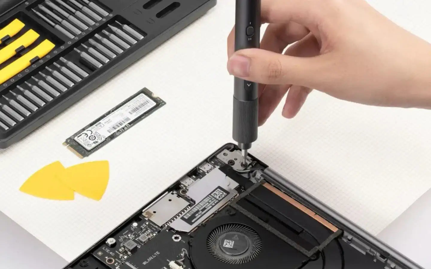Ręka naprawiająca laptopa z zestawem precyzyjnych narzędzi i dyskiem SSD na białym tle