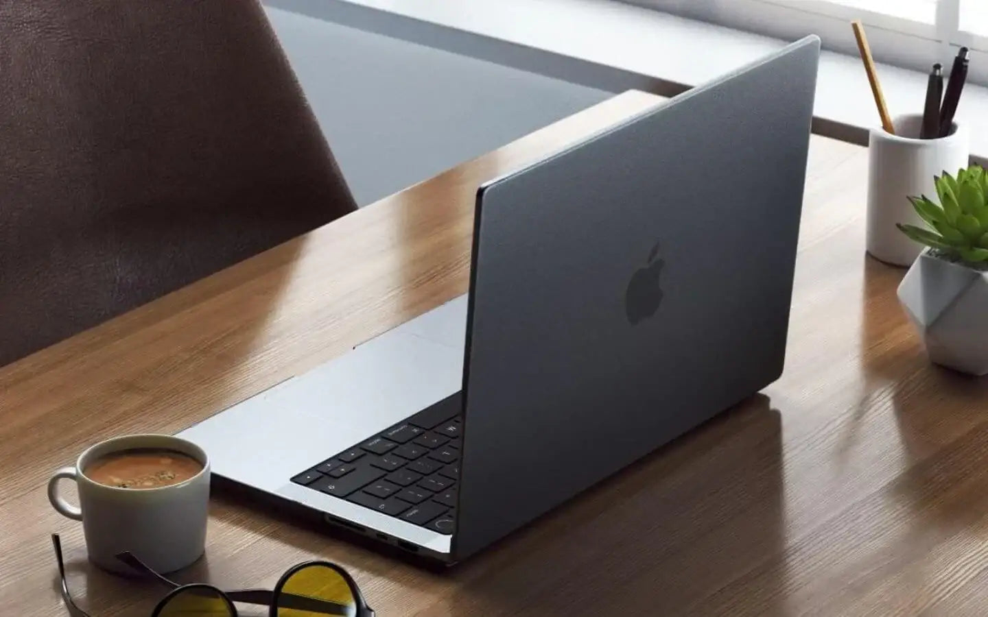 Laptop Apple na drewnianym biurku z kubkiem kawy, okularami i zieloną rośliną