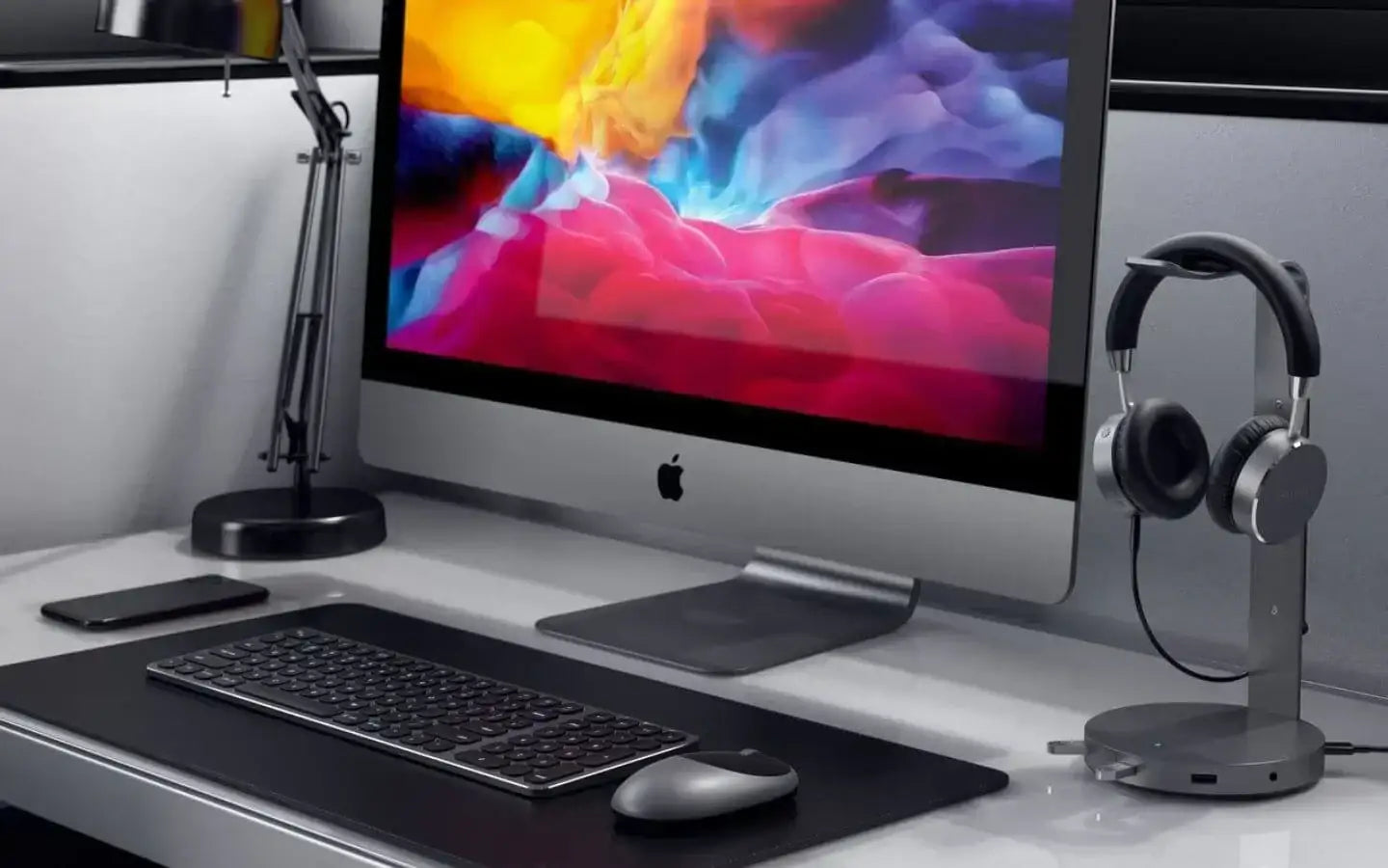 Nowoczesne biurko z komputerem iMac, klawiaturą, myszką, lampką i słuchawkami na stojaku