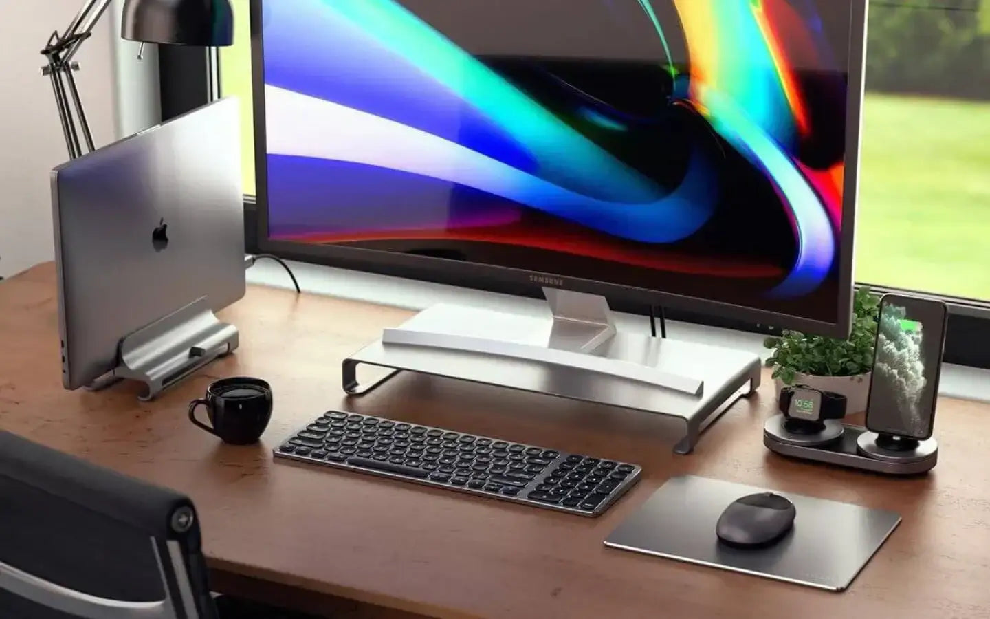 Nowoczesne biurko z monitorem Samsung, stojakiem na MacBook, bezprzewodową klawiaturą i myszką oraz stacją ładującą Apple Watch i iPhone
