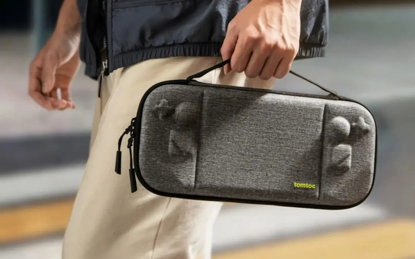 Torba przenośna tomtoc na akcesoria, szara, z uchwytem, trzymana przez osobę w beżowych spodniach