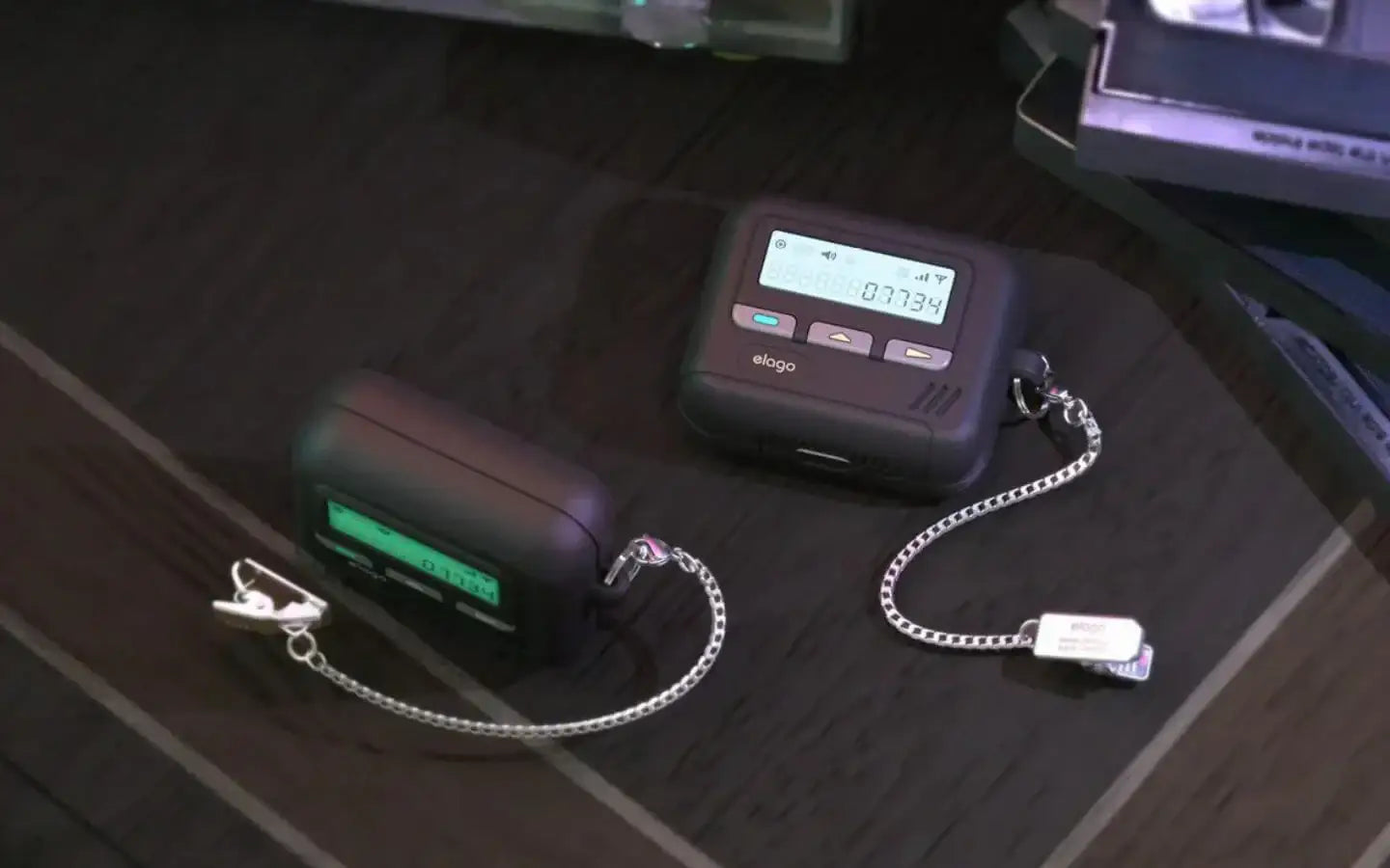 Etui elago do AirPods w stylu retro pagera na ciemnym drewnianym blacie, srebrny łańcuszek.