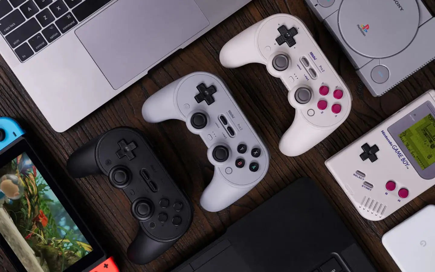 Konsolowe kontrolery, Nintendo Game Boy, PlayStation Classic i laptopy na drewnianym stole
