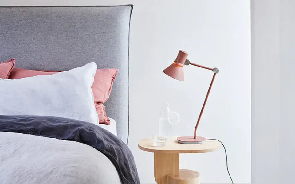Różowa lampka Anglepoise Type 80 na drewnianym stoliku nocnym obok łóżka w sypialni