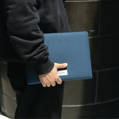 Osoba trzymająca granatową etui Native Union na laptopa, idealne akcesorium do domowego biura
