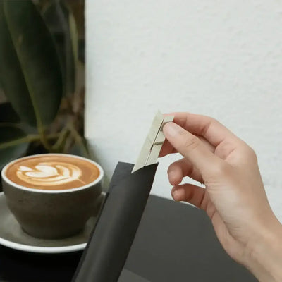 Ręka wyjmująca jasne naklejki klawiszy z czarnej maty obok filiżanki kawy latte z dekoracją w kawiarni