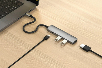 Srebrny hub USB-C 4w1 z podłączonymi pendrive'ami i kablami na biurku obok laptopa