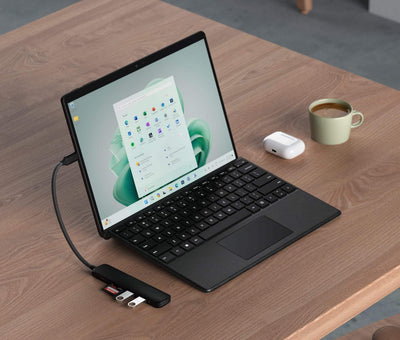 Nowoczesny laptop z podłączonym hubem USB-C na biurku, widoczne pendrive'y i karta SD