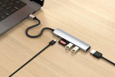 Srebrny hub USB-C z wieloma portami, podłączony do laptopa na drewnianym biurku