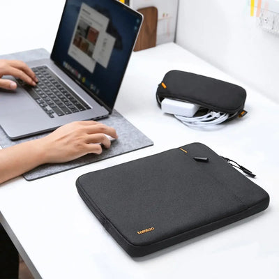Czarna torba na laptopa i organizer na kable na biurku obok pracującej osoby, akcesoria do home office