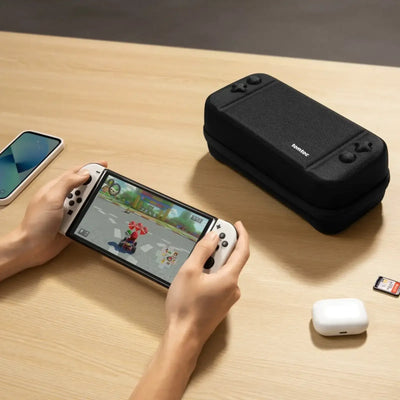 Gracz trzyma konsolę Nintendo Switch OLED, etui i akcesoria na biurku, desk setup gamingowy.