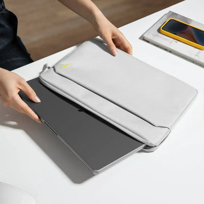 Szara etui na laptopa na biurku, osoba wkłada nowoczesny laptop, obok telefon i notatnik.