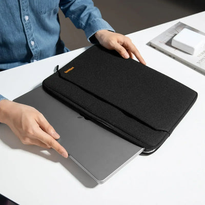 Czarna torba na laptopa, osoba wkłada srebrny laptop na biurku w home office