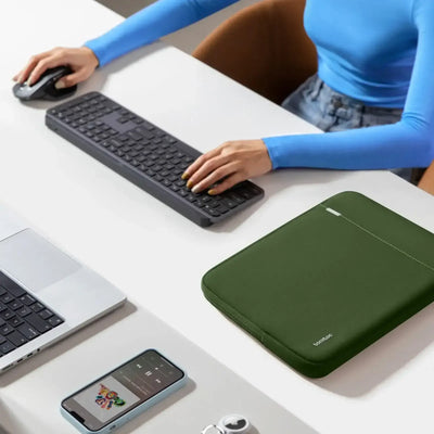 Nowoczesny desk setup z klawiaturą, myszką, laptopem i zielonym etui na biurku