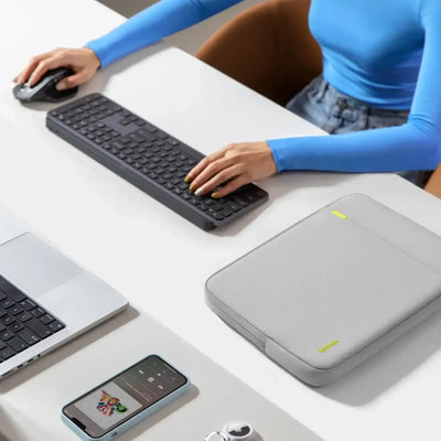 Minimalistyczny desk setup z klawiaturą, myszką, etui na laptopa i smartfonem na biurku