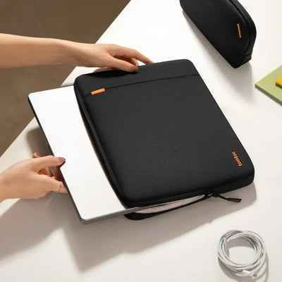 Etui na laptopa czarne na biurku, ręka wkłada MacBooka, akcesoria biurowe w tle